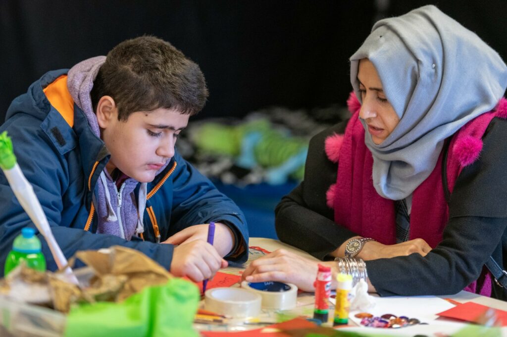 A photo of a carer and a child working on some drawing.